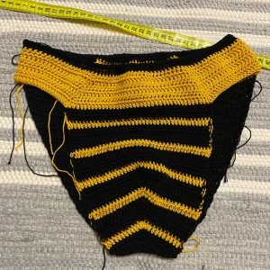 Image showing the meticulous process of crafting crocheted swimwear for men, with a focus on a designer's hands as they skillfully crochet the fabric, highlighting the detailed stitches and the quality of the yarn used.