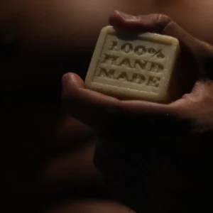 Male hand holding a handmade olive oil soap bar against a bare chest