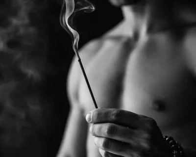 Man holding incense stick with rising smoke in a calm, minimalist setting