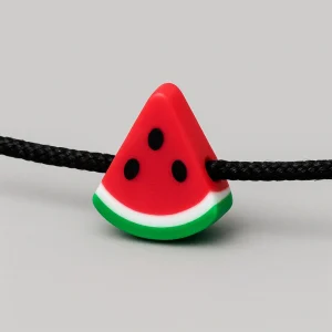 Close-up of a watermelon charm on a black cord Free Palestine bracelet on a light grey background